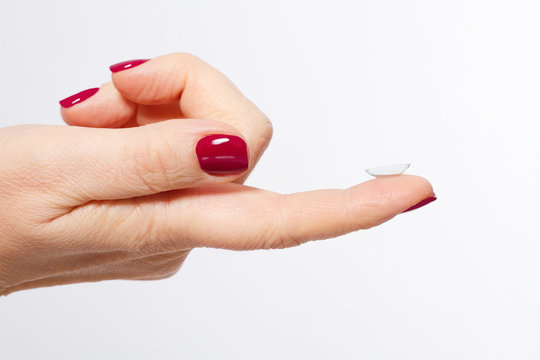 Female finger with red manicure and contact lens isolated on white background. Close-up and selective focus. Copy space and mock up