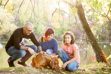 Gorgeous family of father, mother and daughter on the riverside playing with their dog. Animal lovers
