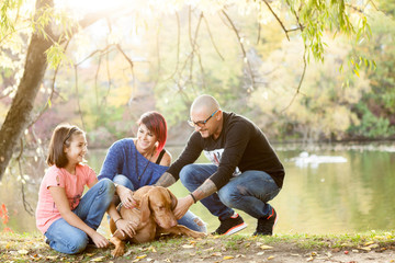 Gorgeous family of father, mother and daughter on the riverside playing with their dog. Animal lovers