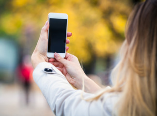 Woman taking picture with smartphone in colorful autumn street