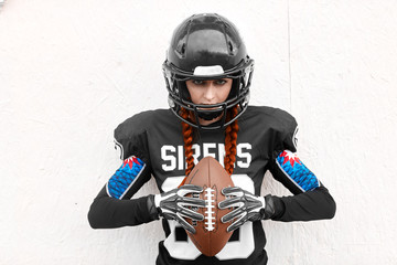 Girl American football player standing with ball on white background.