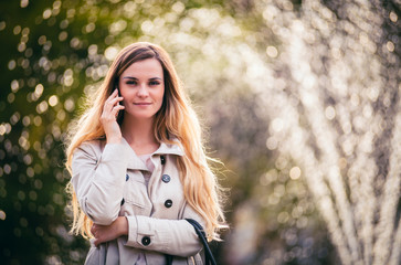 Smiling woman wearing coat walking in city and using smartphone