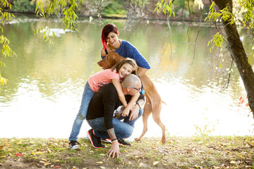 Happy gorgeous family of father, mother and daughter on the riverside playing with their dog. Animal lovers