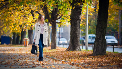 Obraz premium Smiling woman in coat walking on beautiful autumn street