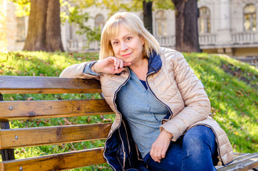   Middle-aged blond woman sitting on a  bench in the park looking at the camera on the autumn...