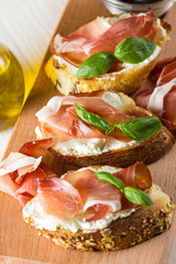 Italian tomato, prosciutto, jamon, ham and cheese bruschetta. Tapas, antipasti with chopped vegetables, herbs and oil on grilled ciabatta and baguette bread.