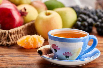 a cup of tea with cinnamon, tangerine, apples, pears, pomegranate and grapes on a wooden table