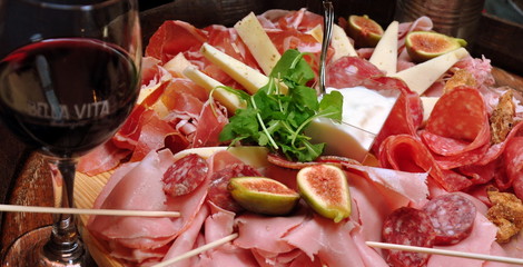Rundes Holzbrett mit leckerem Schinken, Salami und Käse sowie Spießchen und einem Glas Rotwein im...