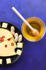 Hard cheese with holes on a black plate, cheese with peanuts, honey, biscuits, walnuts, cheese in minimalism style, cheese on dark blue background