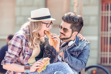 Young couple sharing a sandwich outdoor.