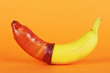 Banana with condom on colored background, close up. Contraceptive concept.