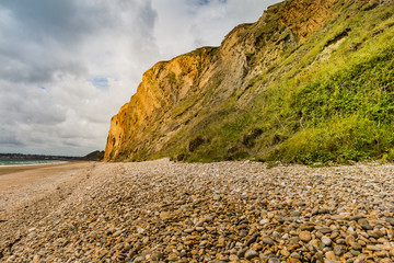 The pebble beach and vegetation surrounding Red Cliff in Yaverland, Sandown, Isle of Wight, England on a stormy cloudy day.