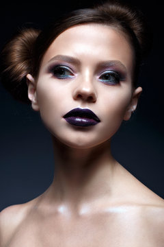 Young girl with creative makeup and hairdo. A beautiful model with bright eyes and purple lips. Shining skin. Beauty of the face. Photo taken in the studio