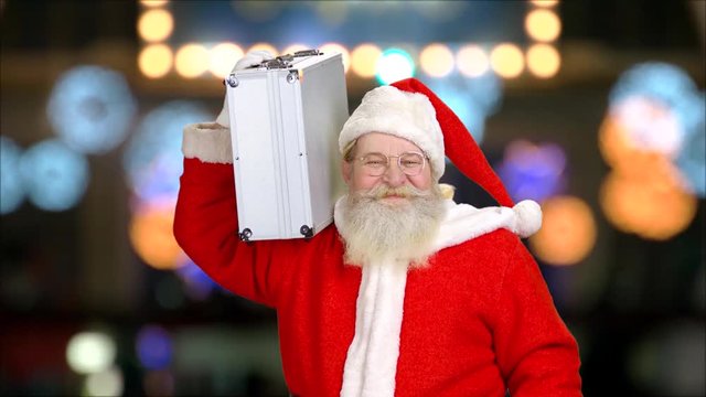Cheerful Santa Claus holding briefcase. Santa on bokeh background.