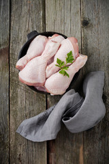 Raw chicken legs on a cast iron pot with spices and herbs on old wooden background prepared for cooking. Selective focus. Top view. Copy space.