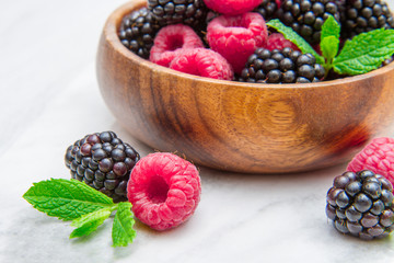 Wooden cup with fresh berries on white marble background 