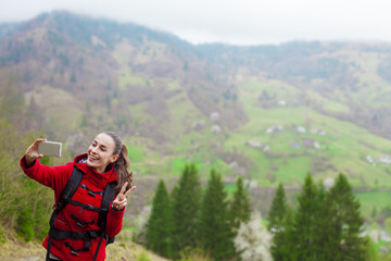 Young smiling woman tourist taking pictures of herself and nature in the mountains
