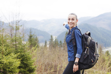 Young smiling tourist woman with a backpack in the mountains enjoying the scenery