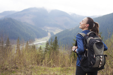 Young smiling tourist woman with a backpack in the mountains enjoying the scenery