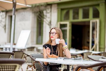 Young woman smoking a cigarette while having a breakfast outdoors at the typical french cafe terrace in France