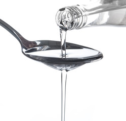 Coconut oil pouring from a bottle to spoon over white background