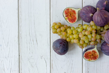 Fresh and ripe fig and grape fruits over white wooden board.