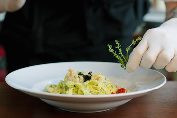 Chief dressing pasta with black truffle and herbs.