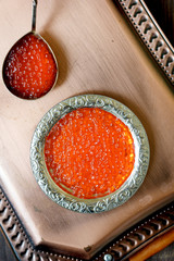 Top view of red caviar inside metal plate over copper tray.