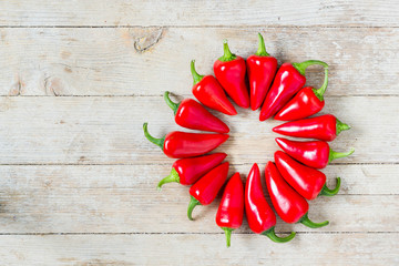 Red jalapeno peppers in wheel, round shape on wooden background, top view.