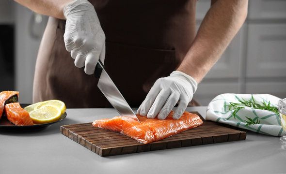 Man cutting fresh salmon fillet in kitchen
