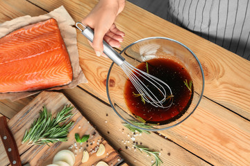 Woman preparing soy marinade for salmon on wooden table