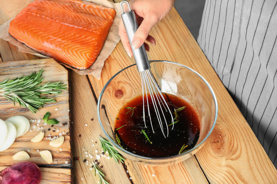 Woman preparing soy marinade for salmon on wooden table