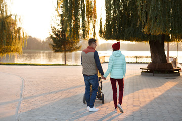 Back view of young loving couple holding hands. Parents with baby pram in autumn park. Love, parenthood, family, season and people concept.