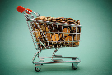 Shopping trolley with coins on a green background