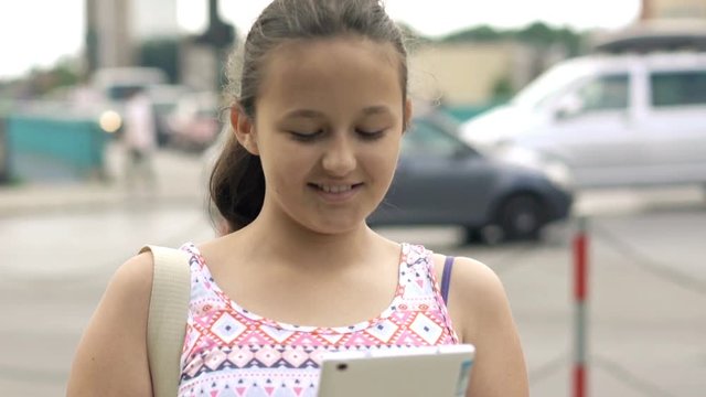 Young teenager girl using tablet computer standing near street in city
