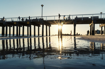 Sunburst under a pier on the beach with silhouetted people above and below