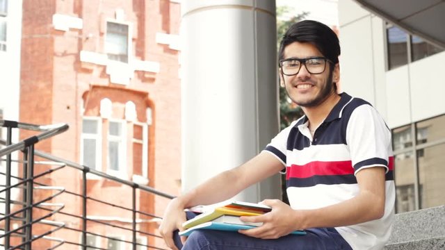Portrait of a smiling male asian student sitting on stairs and reading book