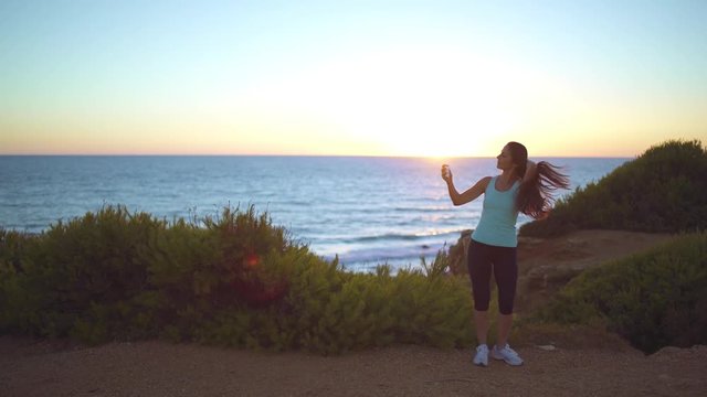 Running woman watch the sea and takes a photo in a beautiful place at sunset