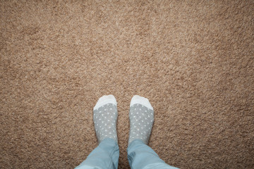 Female feet in warm socks against a background of brown carpet, space for text.