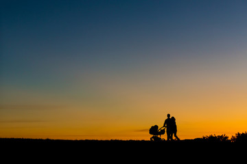Obraz na płótnie Canvas Sillhouette of a young couple walking during sunset with a baby in the stroller