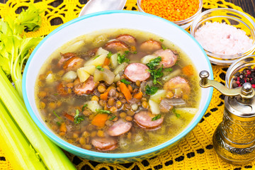 Soup with lentils, celery and sausages on old wooden table
