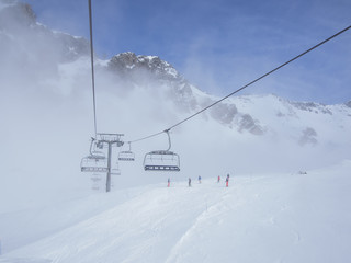 Fototapeta premium Chair lifts, skiers, and mountain peaks emerge from the fog