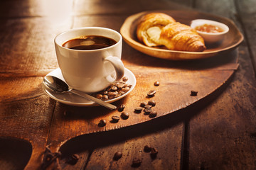 Cup of coffee with croissant on wooden board