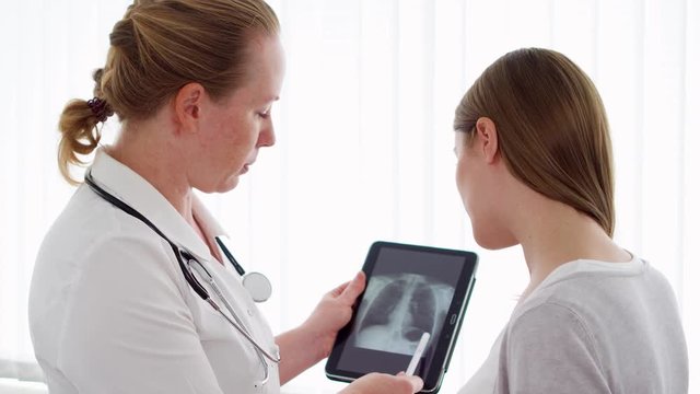 Woman physician with stethoscope talking with female patient in clinic. Female professional doctor at work. Showing X-ray on tablet. Health care