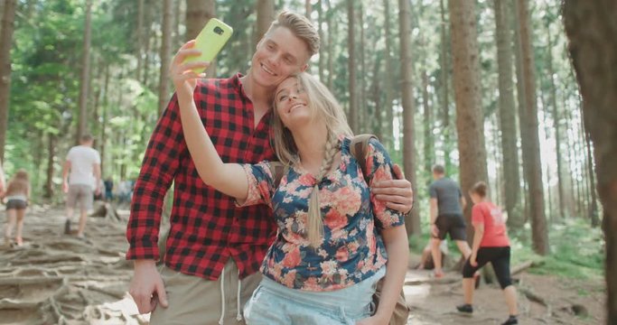 Loving young caucasian couple taking self portrait in a forest. Man and woman on vacation taking selfie with their smartphone.