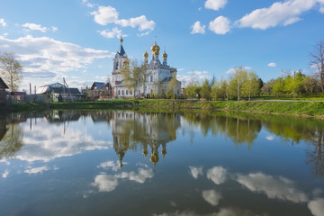 Fototapeta na wymiar Landscape with an Orthodox church on the shore of the pond on the May day. The Church of the Intercession of the Blessed Virgin Mary in the village of Zhestylevo, Dmitrovsky District, Moscow Region