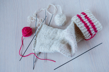 Knitted sock, knitting needles and coats of wool on the table