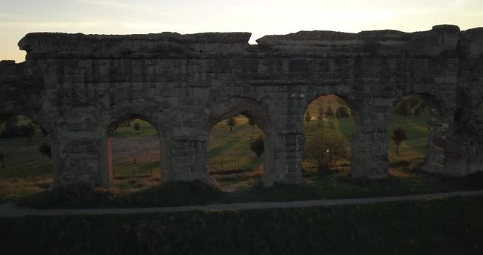 Video from above. Aerial view of the ancient Roman Aqueduct at sunset. Old ruins surrounded by a green public Park. Rome, Italy.
