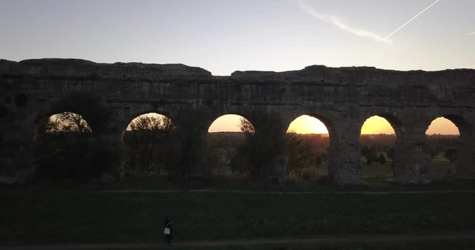Video from above. Aerial view of the ancient Roman Aqueduct at sunset. Old ruins surrounded by a green public Park. Rome, Italy.