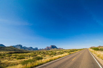 A road runs through Big Bend National Park, West Texas, and passes Chisos mountains before disappearing in to the wide open blue sky. Escape and wanderlust metaphor